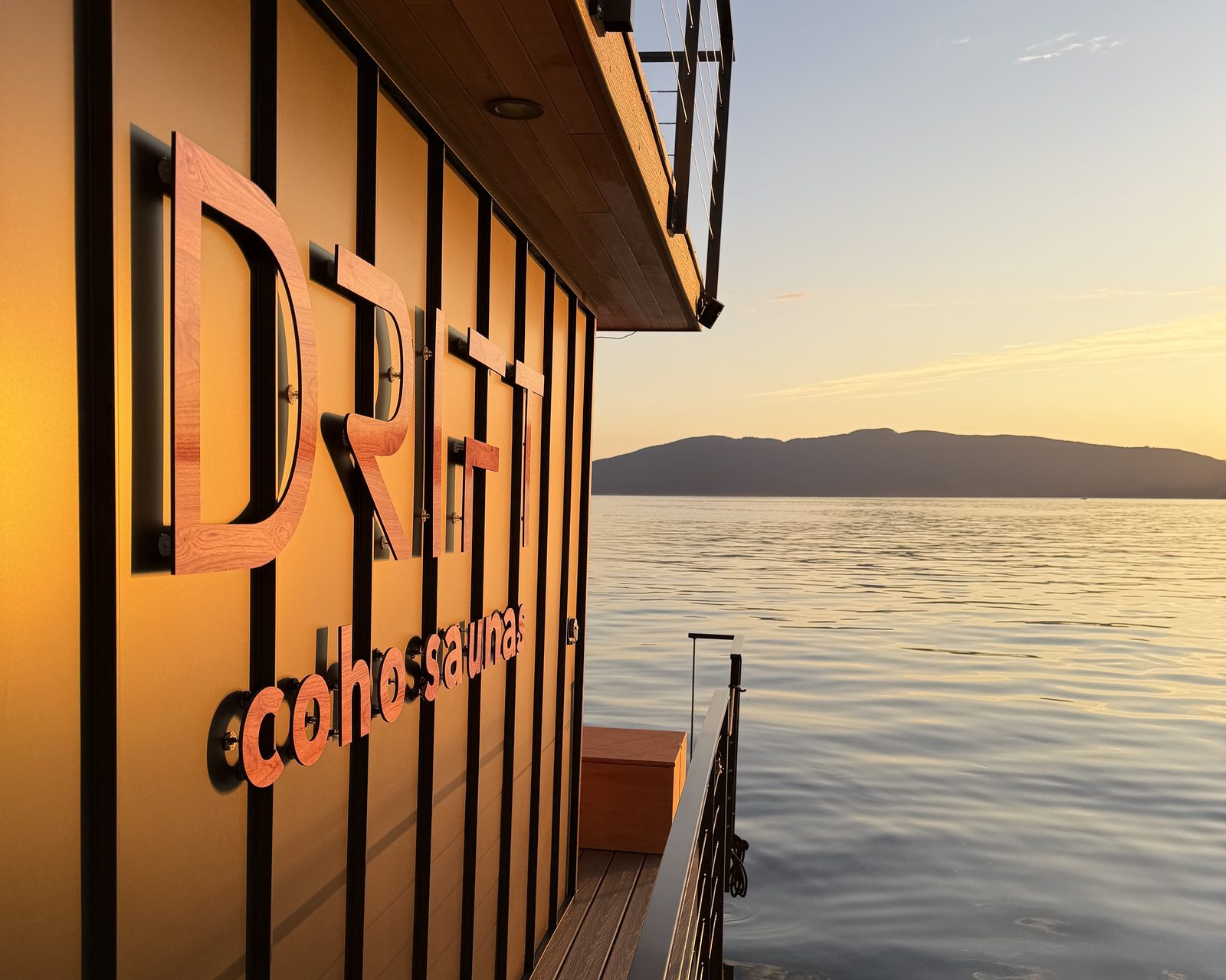 The Drift's cedar lettering glowing along the hull at sunset, Bellingham Bay and the islands beyond