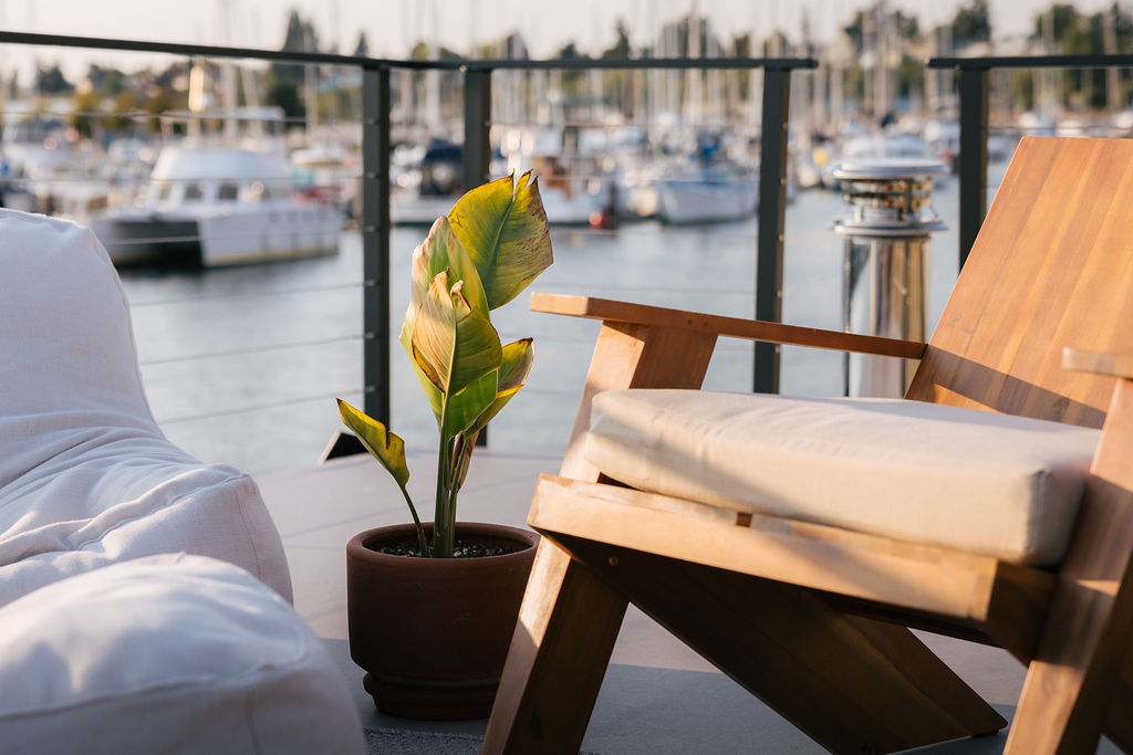 Wooden lounge chair and potted plant on the rooftop deck, marina boats beyond the rail
