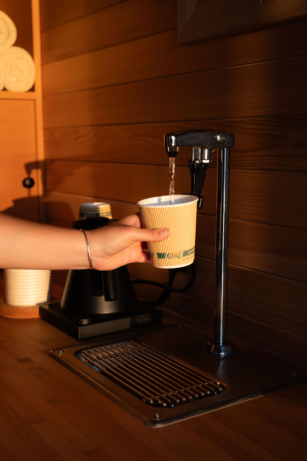 A cup filling at the hot-water tap in the cedar-lined tea station
