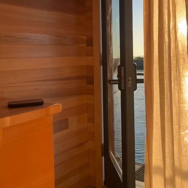 Low sun pouring through the open sauna door and linen curtain, the bay just outside