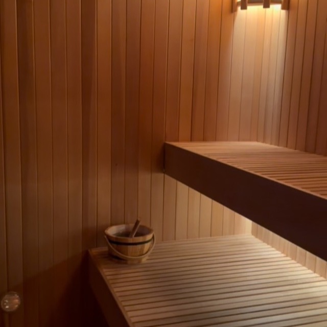 Inside the cedar sauna — warm-lit benches and a wooden water bucket